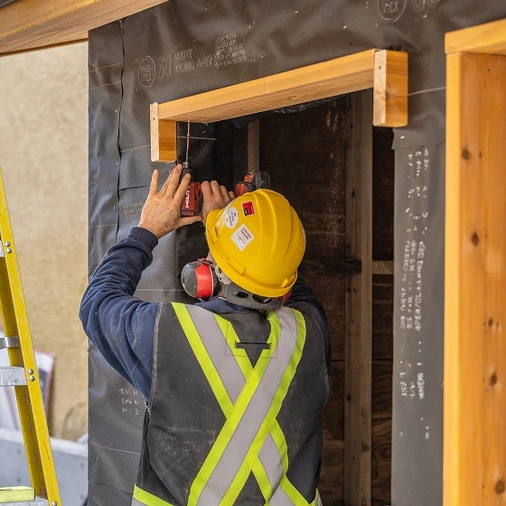 Worker in a yellow hard hat and safety vest fitting a cedar door frame