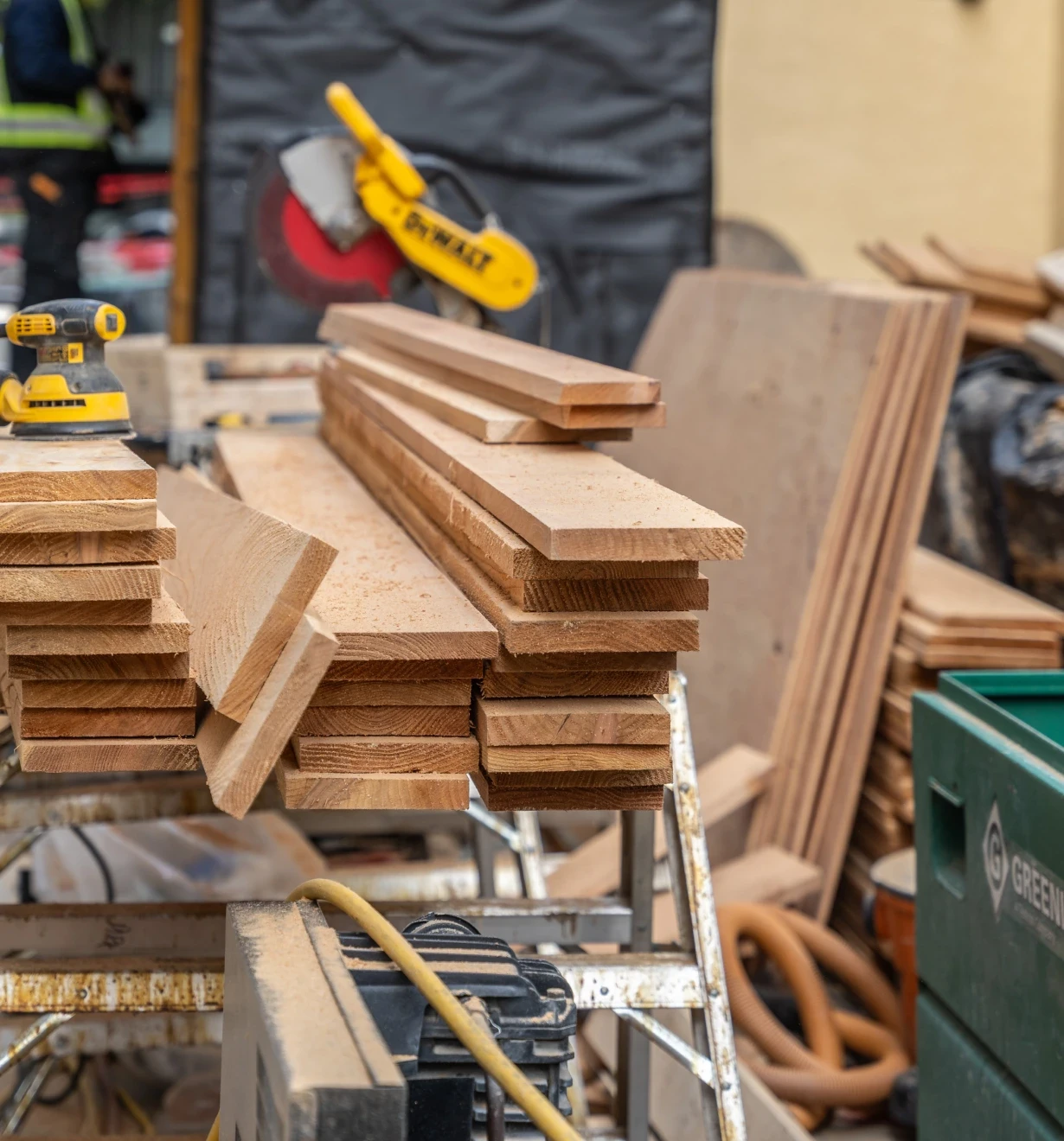 Stacked cedar boards on a sawhorse beside a mitre saw on a job site