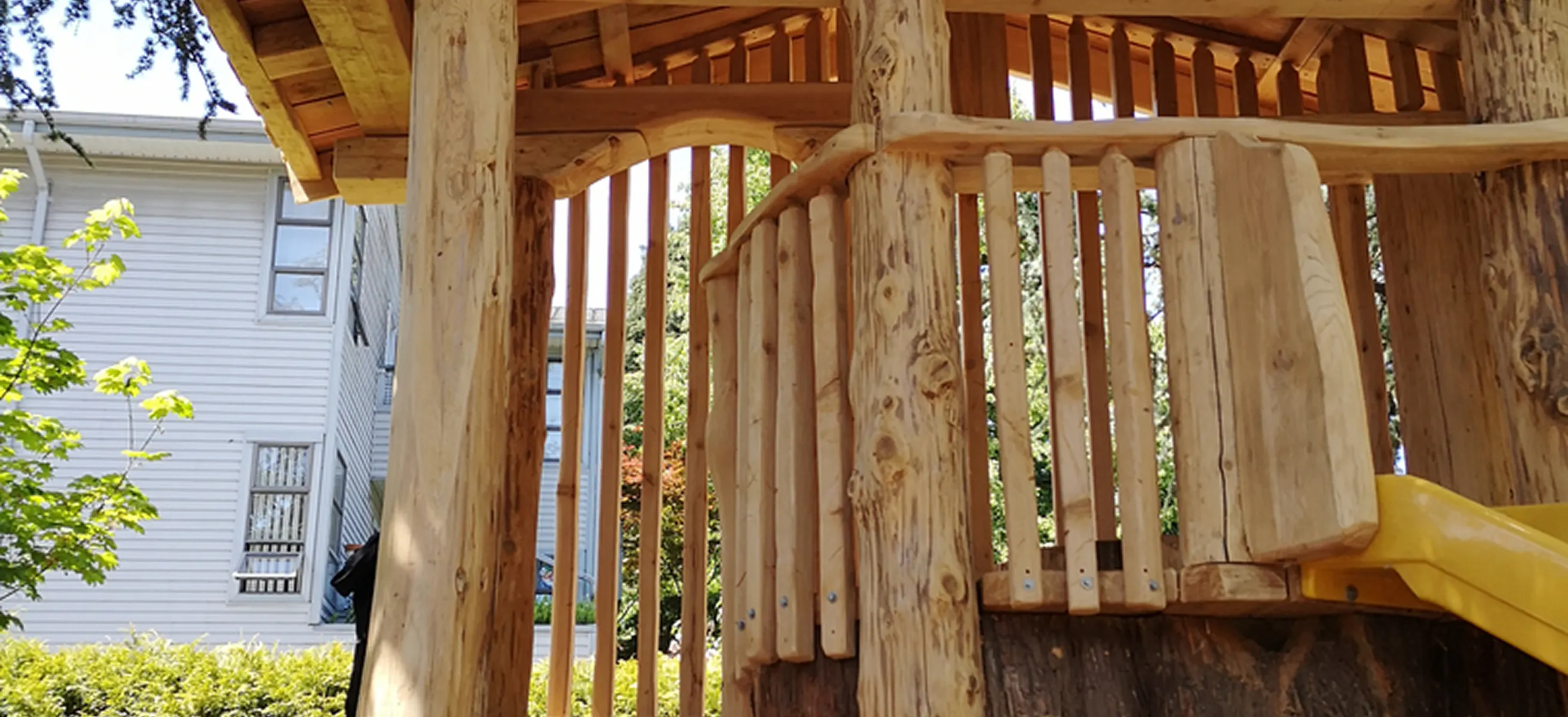 Close view of a log play structure with peeled-log posts, slatted walls and a yellow slide