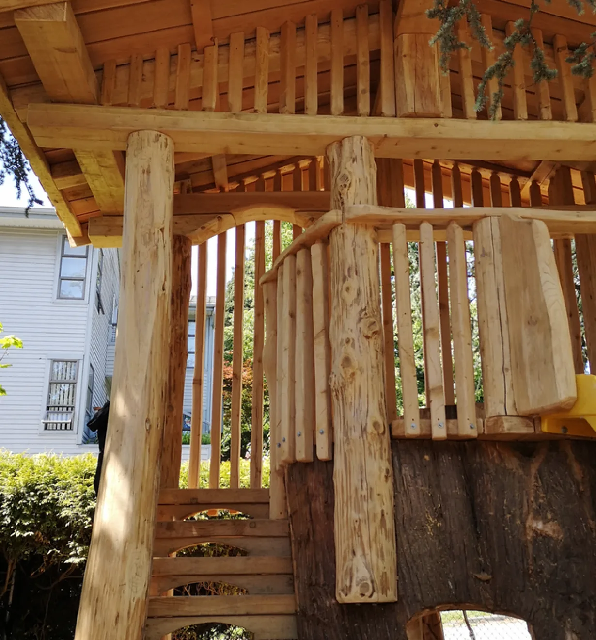Underside of a log play structure with peeled-log posts, wooden slat walls and a timber roof