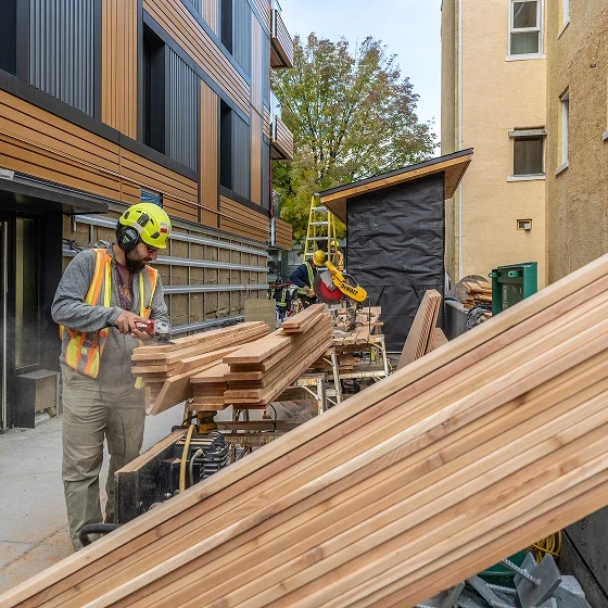 Worker in a hard hat and safety vest cutting cedar boards in a construction laneway