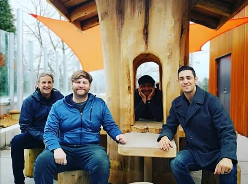 Four members of the Dirks team seated around a live-edge table beside a carved tree trunk
