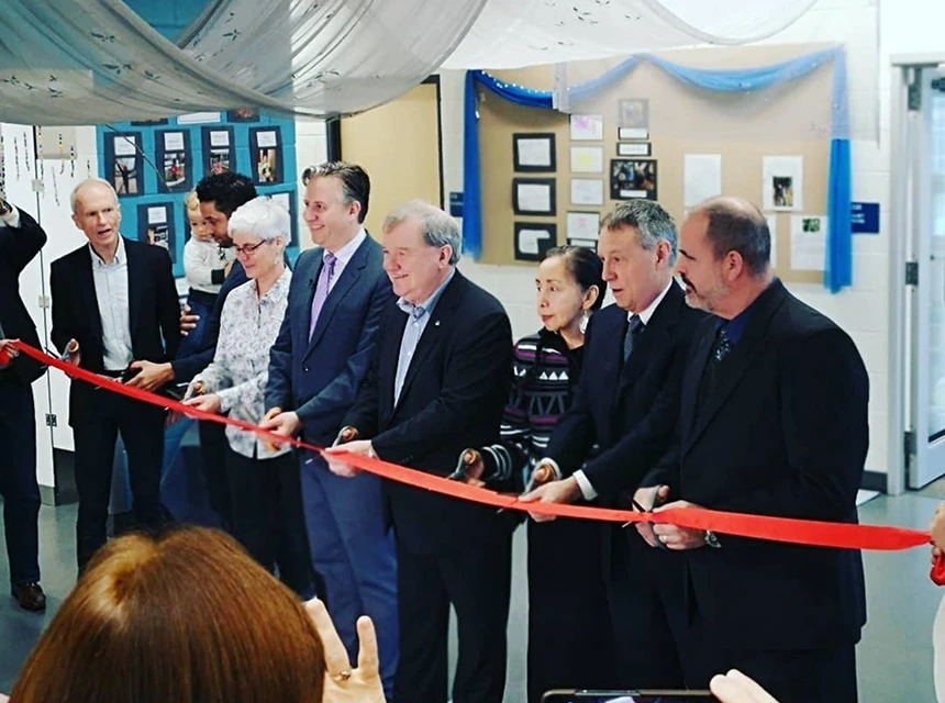 Group of people in a classroom cutting a red ribbon together