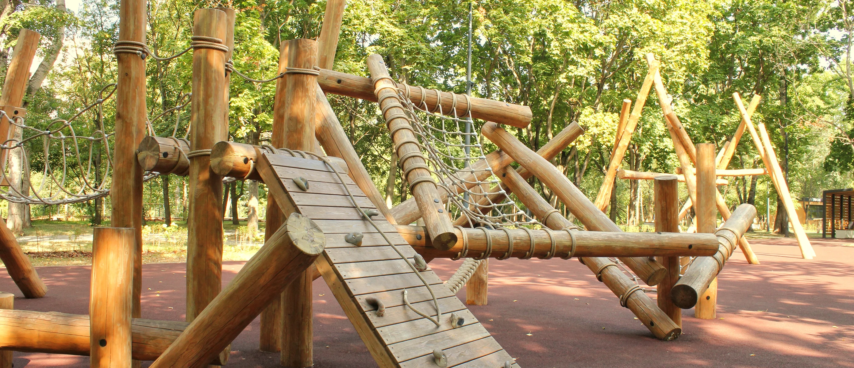 Log climbing frame with rope net and slatted wooden ramp on red rubber safety surfacing