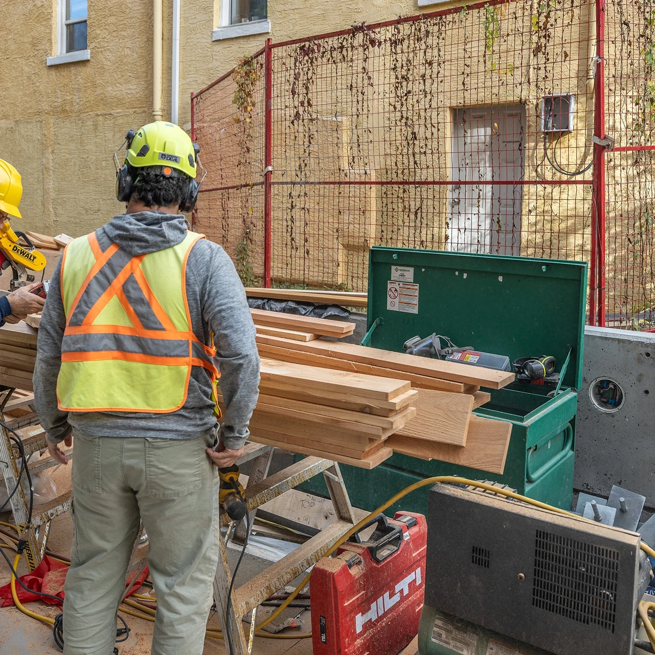Worker in a hard hat and safety vest beside stacked lumber and tools on site