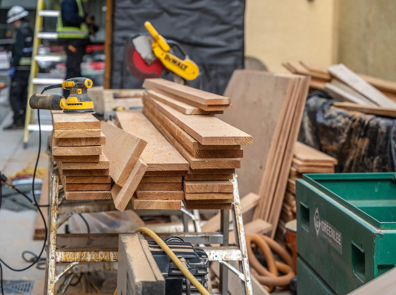 Stacked cedar boards on a sawhorse beside a mitre saw on a job site